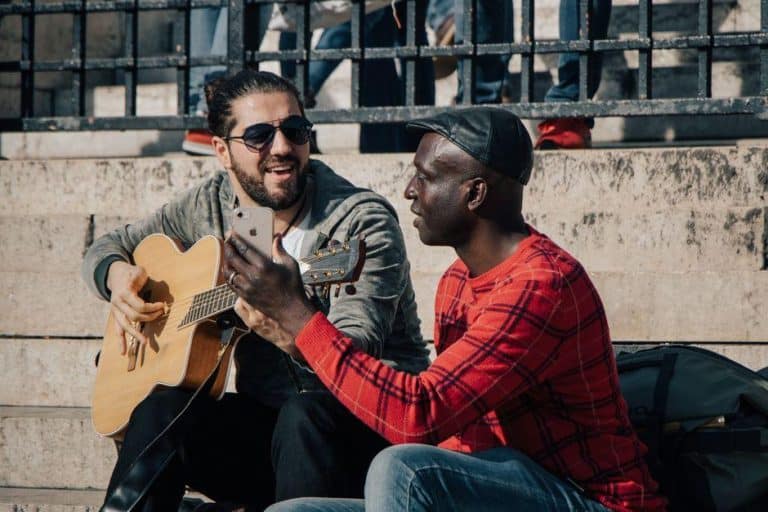 Deux guitaristes en plein air, l'un joue de la guitare acoustique pendant que l'autre filme avec son smartphone