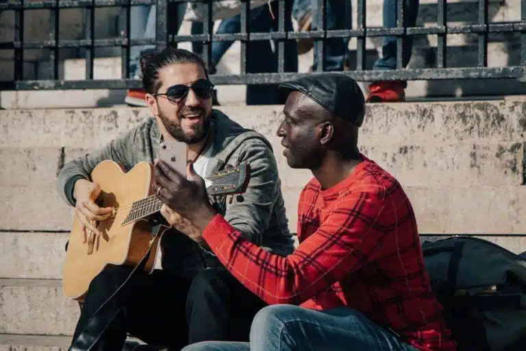 Deux guitaristes en plein air, l'un joue de la guitare acoustique pendant que l'autre filme avec son smartphone