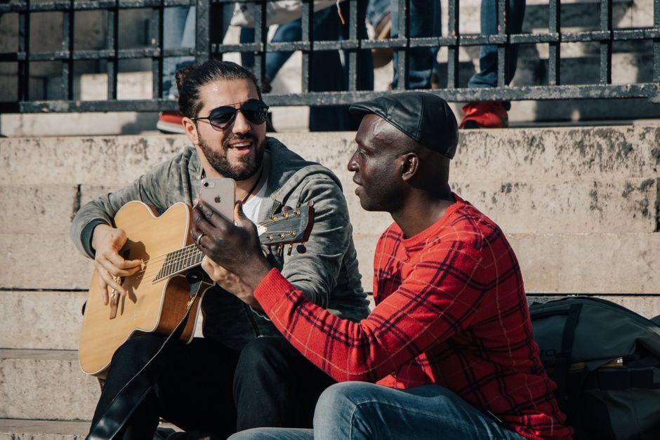 Home 5 Deux guitaristes en plein air, l'un joue de la guitare acoustique pendant que l'autre filme avec son smartphone
